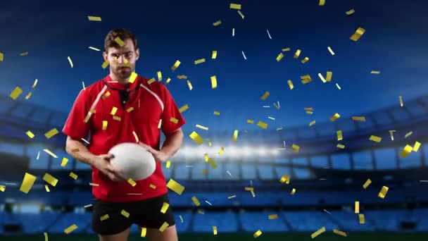 Animation of a Caucasian male rugby player playing with a ball and looking to camera with golden confetti falling and a floodlit sports stadium in the background - Materiał filmowy, wideo