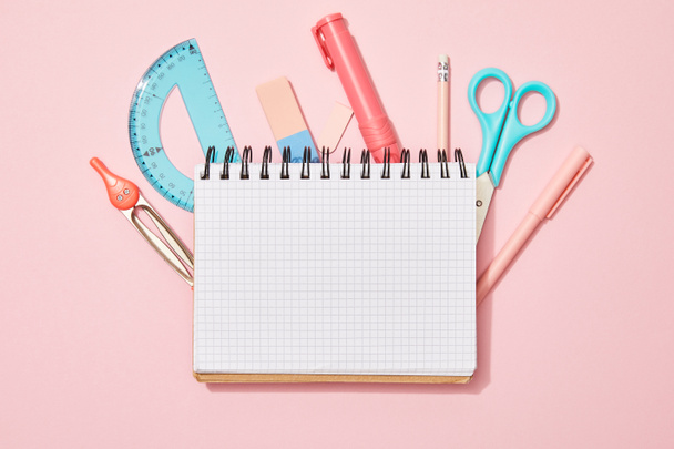 top view of blank notebook among school supplies on pink background - Фото, изображение