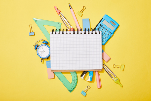 top view of school supplies scattered on yellow background with empty notebook - Фото, зображення