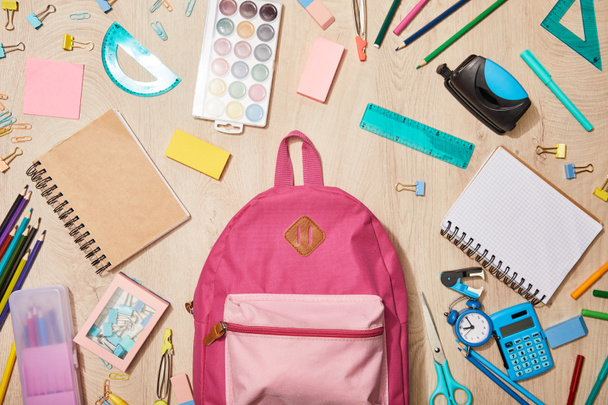 ahşap masa üzerinde pembe sırt çantası ile çeşitli okul malzemeleri üst görünümü - Fotoğraf, Görsel