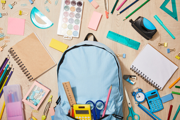 Widok z góry na różne materiały szkolne z niebieskim plecakiem na drewnianym biurku - Zdjęcie, obraz