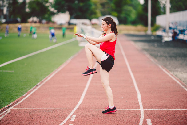 Female athlete preparing legs for cardio workout. Fitness runner doing warm-up routine. woman runner warm up outdoor. athlete stretching and warming up on a running track in a stadium - Photo, Image