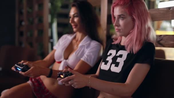 Two sexy girls playing tv game holding joysticks - Filmati, video