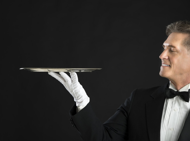 Mature Waiter Smiling While Looking At Serving Tray - Photo, Image