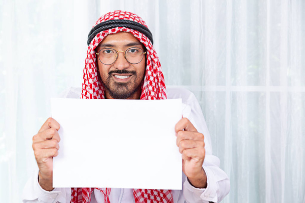 glücklicher arabischer saudi Mann lächelt und zeigt ein Banner auf weißem Hintergrund. - Foto, Bild