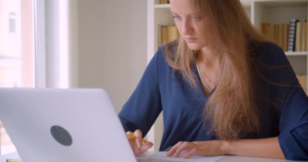Closeup portrait of young attractive caucasian businesswoman using laptop taking notes in office indoors - Footage, Video