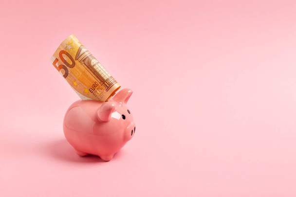 Pink piggy bank with fifty euros on a pink background. - Zdjęcie, obraz