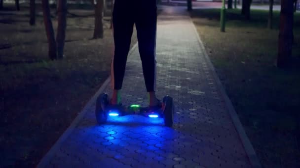 A girl riding a gyro scooter in the evening. Turned on lights in the evening park. Leisure - Кадри, відео
