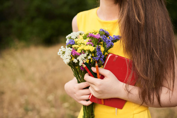 Девушка в парке с цветами, блокнотом и ручкой в руках. Приезжайте в школу. Возвращение в школу - Фото, изображение