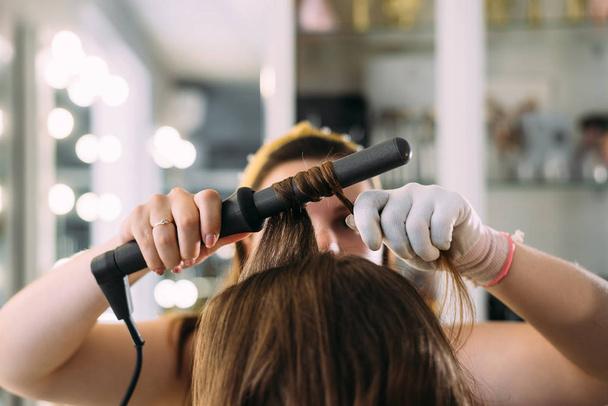closeup hairdresser twists long hair of girl and makes curls - Φωτογραφία, εικόνα