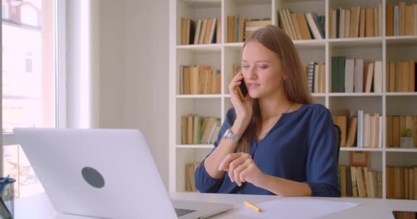 Closeup portrait of young successful attractive caucasian businesswoman using laptop having phone call being unhappy in office indoors - Πλάνα, βίντεο