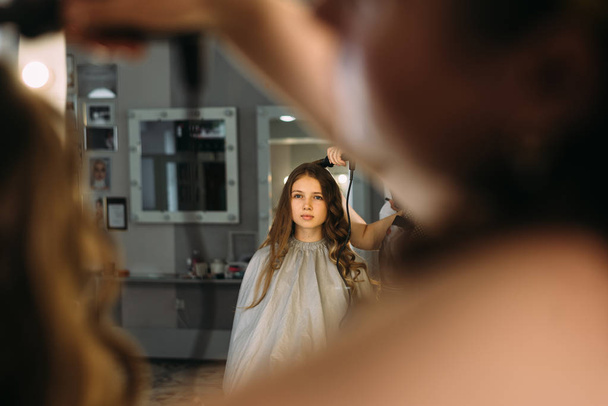 Beauty Studio, een jong meisje zit op een stoel en een kapper. Haar curling proces - Foto, afbeelding