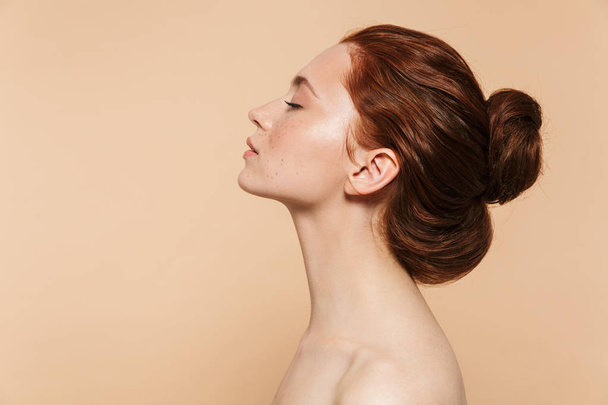 Young redhead woman posing isolated over beige wall background. - Fotó, kép