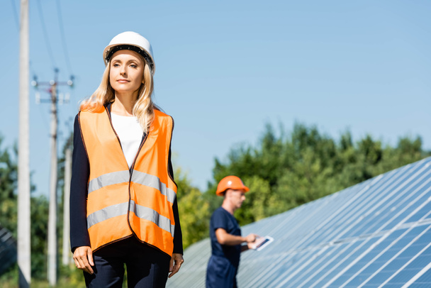 attractive businesswoman in hardhat and safety vest looking away  - Foto, Imagen