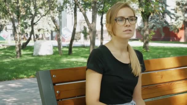 Jonge nerveuze blanke vrouw in brillen wachten op iemand in het stadspark.  - Video