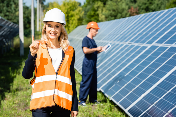 attractive businesswoman in hardhat smiling and showing idea gesture  - Photo, Image