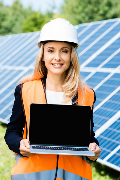 attractive businesswoman in hardhat and safety vest holding laptop with copy space - Photo, Image