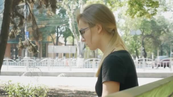 Mladý nervózní kavkazanka v brýlích čekajících na někoho v městském parku.  - Záběry, video