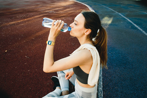 ładna kobieta siedzi na ziemi z butelką wody po jogging na świeżym powietrzu - Zdjęcie, obraz