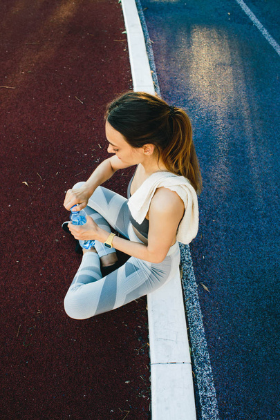 krásná žena, která sedí na zemi s lahví vody po běhání venku - Fotografie, Obrázek