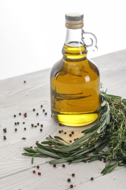 Bottle of oil near rosemary and thyme bungs, scattered red and black peppercorns on white wooden surface isolated on white - Foto, Bild