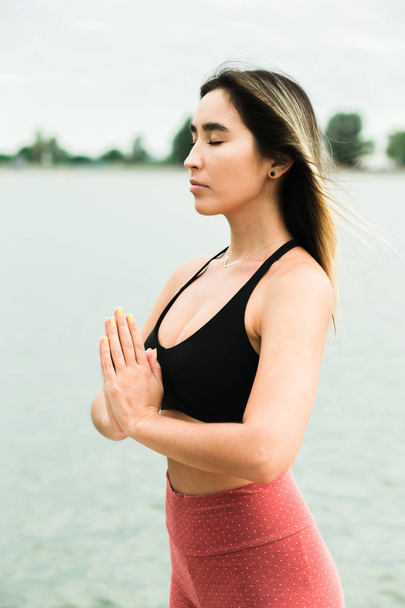 Asian attractive young girl doing yoga outdoors on the pier by the lake. - Photo, Image