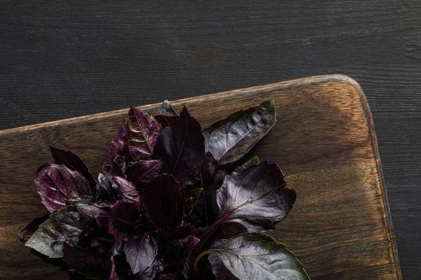 Top view of brown wooden cutting boards with purple basil bundle on dark surface - Photo, Image