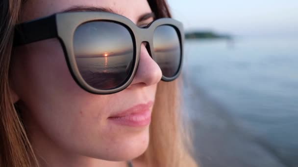 Porträt eines jungen schönen Mädchens mit großer Sonnenbrille in schwarzem Rahmen. das Glas spiegelt den schönen Sonnenuntergang wider. - Filmmaterial, Video