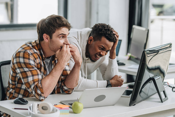 два шокированных мультикультурных программиста смотрят на ноутбук в офисе
 - Фото, изображение