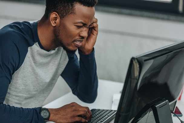 displeased african american programmer looking at computer monitor in office - Photo, Image