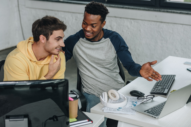 cheerful african american programmer pointing at computer monitor while sitting near colleague - Photo, Image