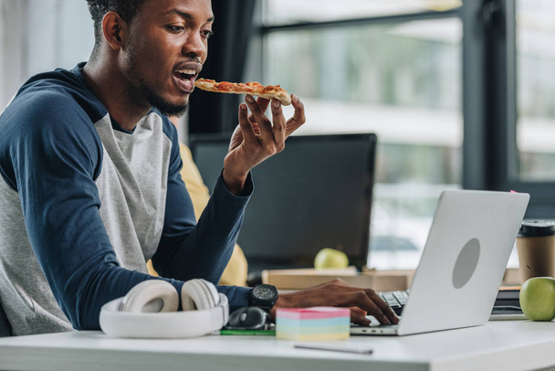 młody African amerykański programista jedzenia pizzy podczas pracy w biurze - Zdjęcie, obraz