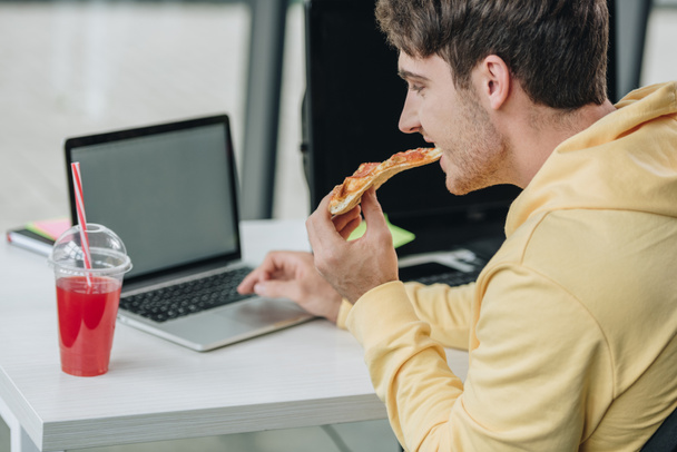 young programmer eating pizza while sitting at workplace in office - Фото, зображення