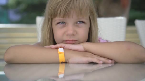Portret van een meisje dat aan een tafel zit met handen gegrepen en naar de camera kijkt - Video
