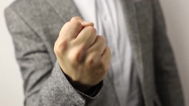Solid caucasian man in gray jacket and speckled shirt on white background pulling fist up. close-up on male fist shaking in front of camera. threat gesture, concept of aggression, warning, punishment - Footage, Video