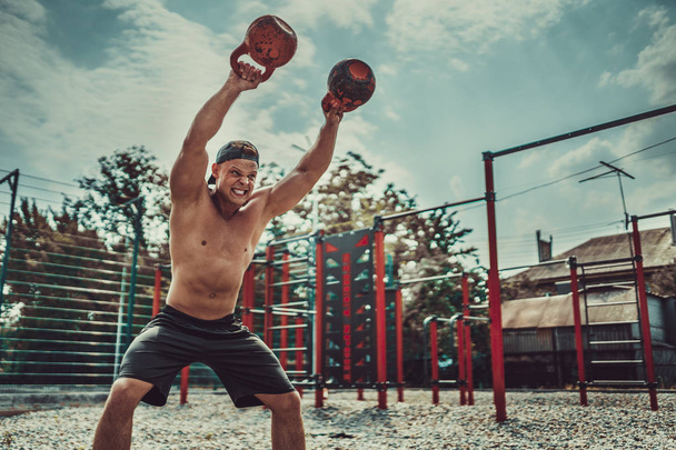 Athletic man working out with a kettlebell at street gym yard. Strength and motivation. - Fotoğraf, Görsel