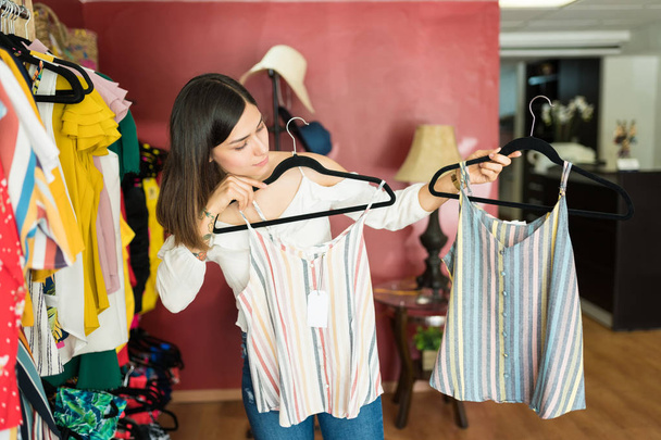 Female customer comparing striped tops hanging from coathangers in shopping mall - Photo, image