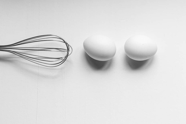 Jajko i trzepaczka na białym tle, czarno-biały monochromatyczny obraz narzędzi do gotowania. Płaski widok z góry - Zdjęcie, obraz