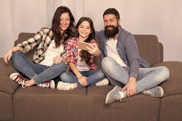 Capture happy moments. Family spend weekend together. Use smartphone for selfie. Friendly family having fun together. Mom dad and daughter relaxing on couch. Family posing for photo. Family selfie - Foto, Bild