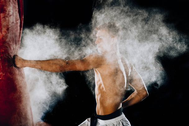 Боец смешанных боевых искусств бьет мешок левой ногой по бокам
 - Фото, изображение