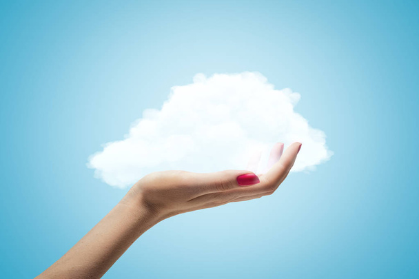 Female hand holding white cloud on blue background - Foto, afbeelding