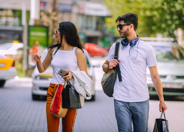 Happy young couple walking together on pavement with shopping bags - Foto, Imagen