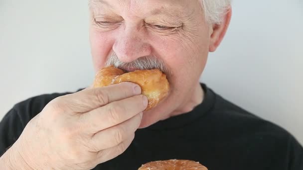 Ο ηλικιωμένος άντρας δαγκώνει σε ένα φρέσκο ντόνατ φούρνου. - Πλάνα, βίντεο