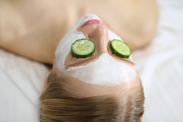Beautiful young woman receiving facial mask of cucumber in beauty salon - Photo, Image