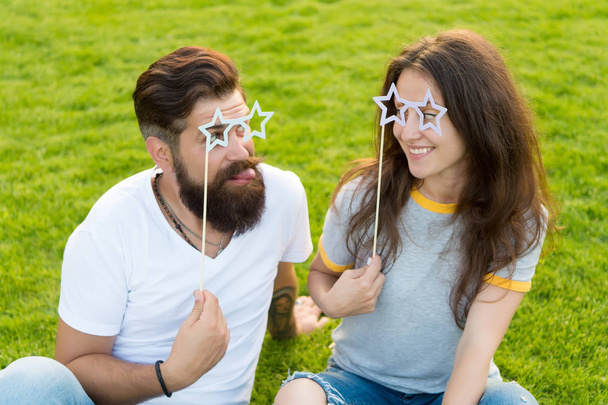 Enjoying funny photo booth. Funny couple looking through prop glasses on green grass. Bearded man and sexy woman making funny grimace on summer day. Funny and playful - Фото, зображення