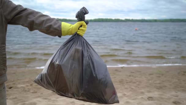 manos voluntarias sosteniendo bolsa de basura en la playa
 - Metraje, vídeo