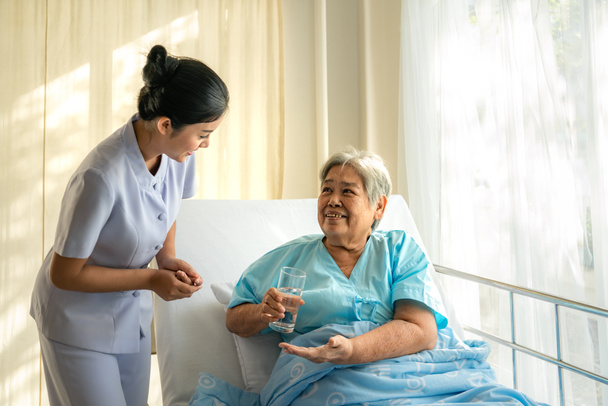 Asijská ošetřovatelka dává starší ženě léky a sklenici vody - Fotografie, Obrázek