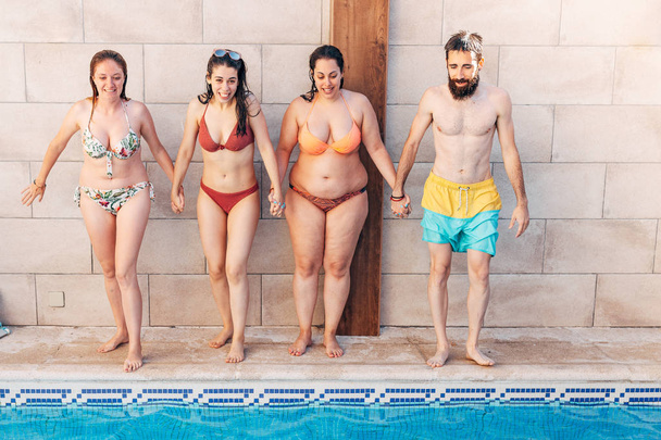 Group of happy friends holding hands and jumping in pool. Young diverse culture people having fun in vacation. Holiday and friendship concept - Foto, Bild