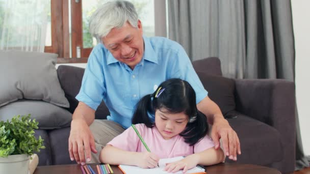 アジアの祖父は孫娘に絵を描いたり、家で宿題を教えています。シニア中国人、おじいちゃんは自宅のコンセプトでリビングルームでソファに横たわっている若い女の子とリラックス。スローモーション. - 映像、動画
