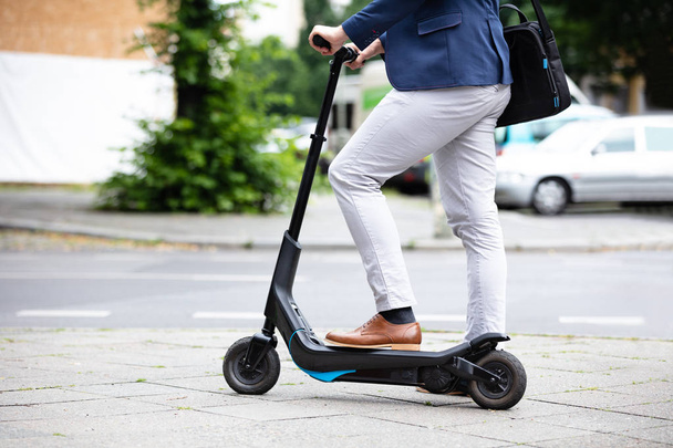 Low Section Of A Businessman Standing On Electric Scooter At Street - Foto, Imagen